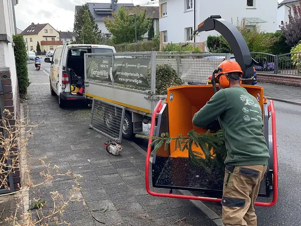 Äste werden in den Häcksler vor dem Firmenwagen gegeben